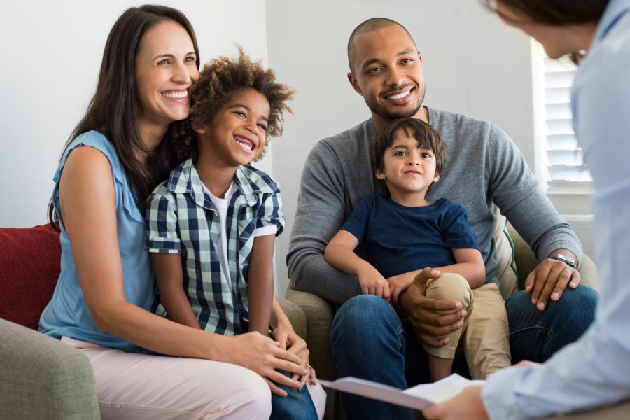 Happy family sitting down together to talk to a women holding paperwork.