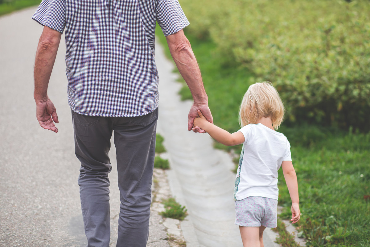 Older gentlemen holding hands with little girl while walking down the street.