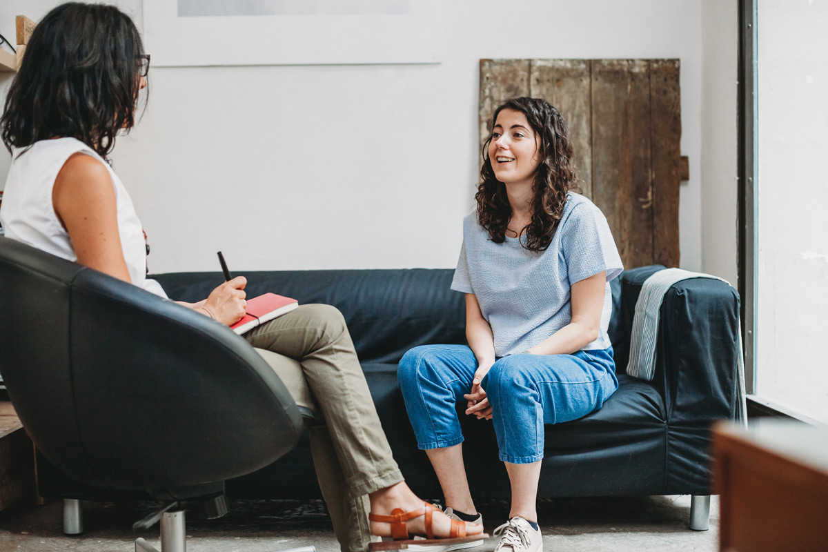 Young women sitting on a couch talking to another women