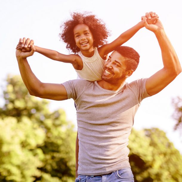 Father carrying daughter on his shoulders while playing outside.