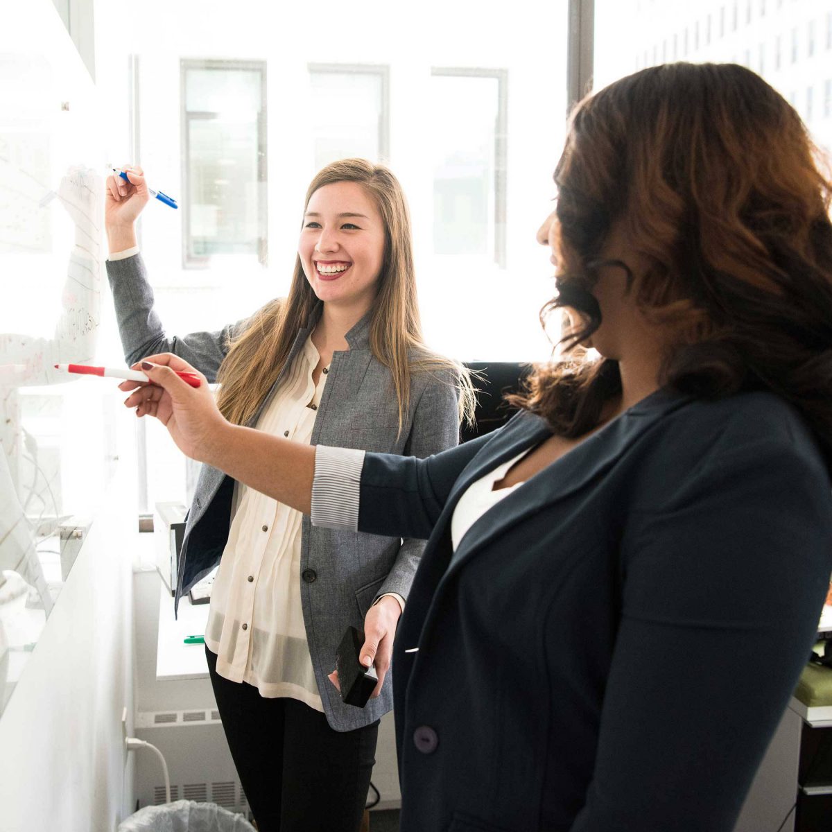 Two women who have signed up to be Workplace Ambassadors with United Way standing at whiteboard talking.