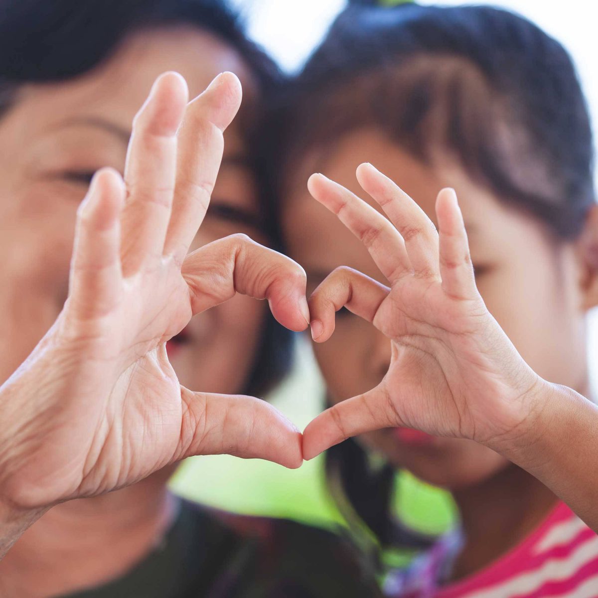 Mother and daughter holding up heart signs together.