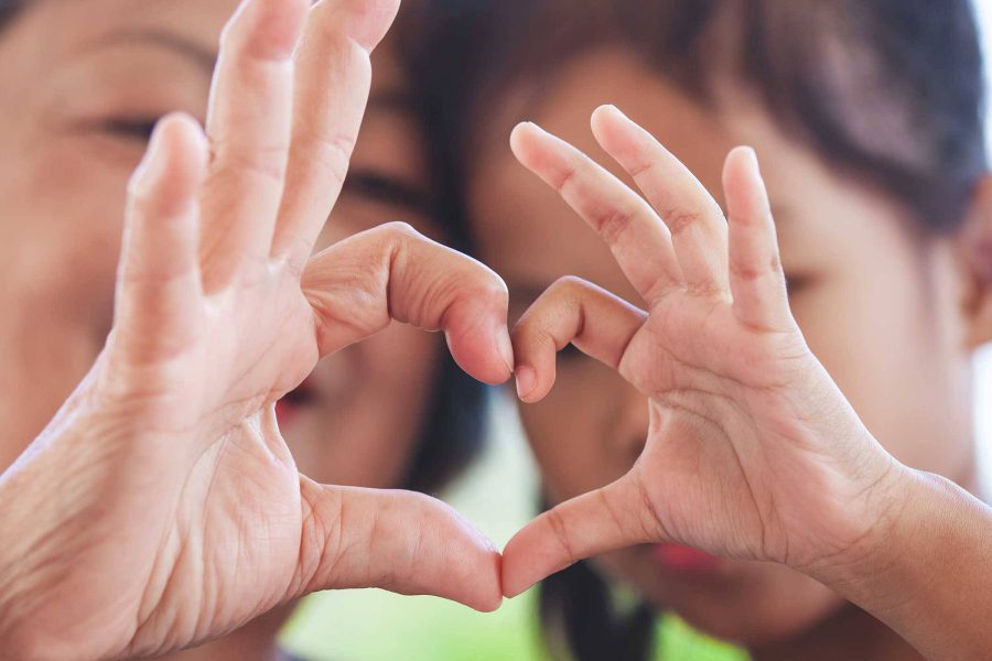 Mother and daughter holding up heart signs together.