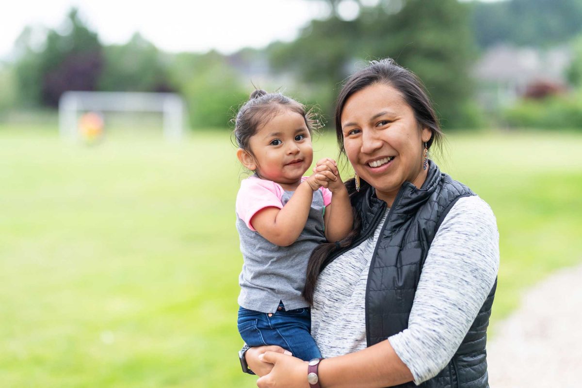 Young mom holding toddler smiling together outside.