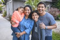 Father and Mother smiling outside with their son and daughter in front of a house.