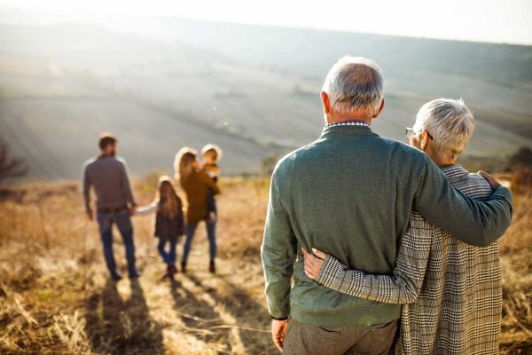 Older couple standing together and admiring their children and grandkids off in the distance.